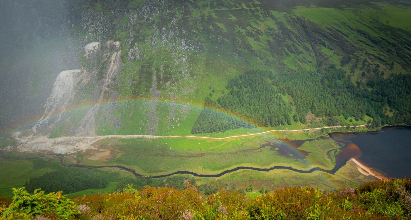 Regenboog over Upper Lake Glendalough met berghellingen op de achtergrond