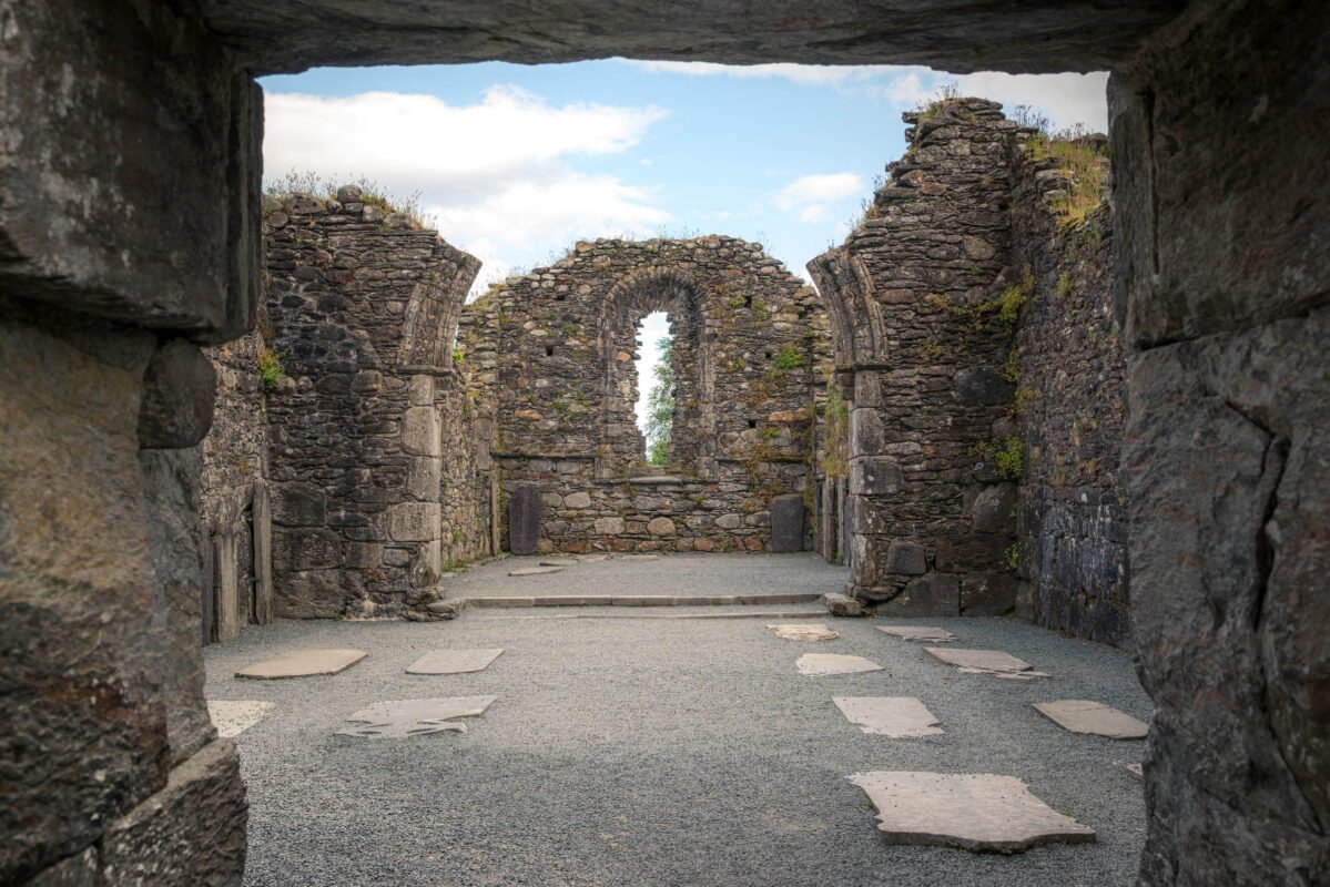 Blik door de stenen ingang van de kathedraal van Glendalough met romaanse bogen en grafstenen op de grond