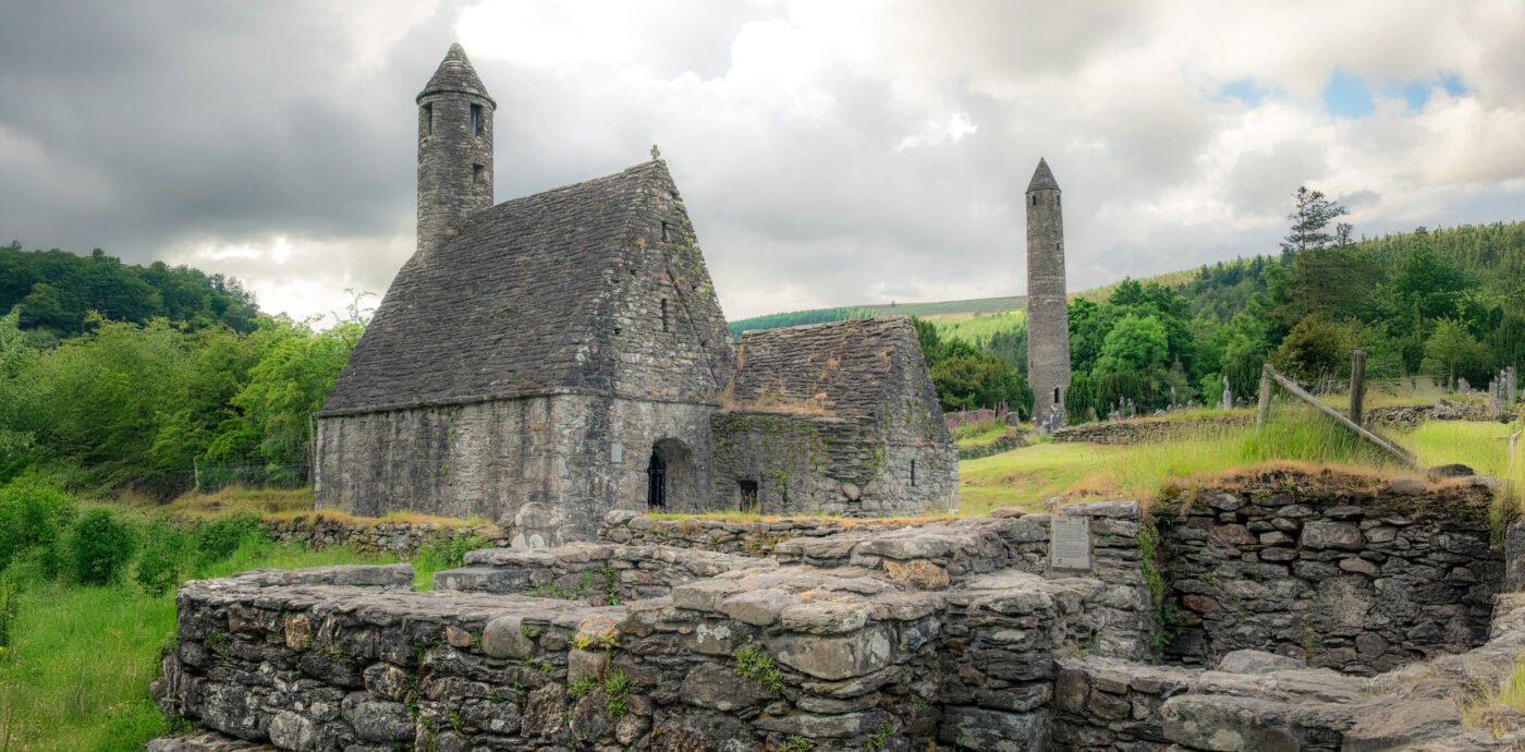 St. Kevin's Kitchen en de Ronde Toren van Glendalough met kerkruïnes op de voorgrond en groene heuvels op de achtergrond